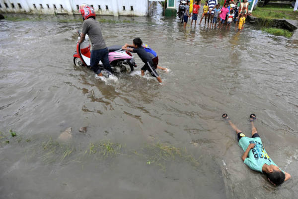 Dua bocah membantu mendorong motor yang mogok ketika melintasi banjir di Syech Yusuf Sungguminasa, Gowa, Sulsel, Selasa (24/12). Hujan selama tiga hari itu mengakibatkan banjir yang merata di Makassar dan Gowa. ANTARA FOTO/Yusran Uccang/ed/Spt/13