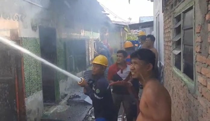 Petugas memadamkan api di rumah kontrakan yang terbakar di Kisaran.