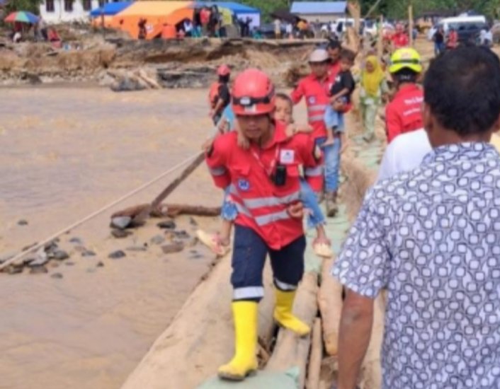ERT Agincourt Resources menggendong seorang anak meniti jembatan darurat yang menghubungkan Tapsel dengan Tapteng. (IST)